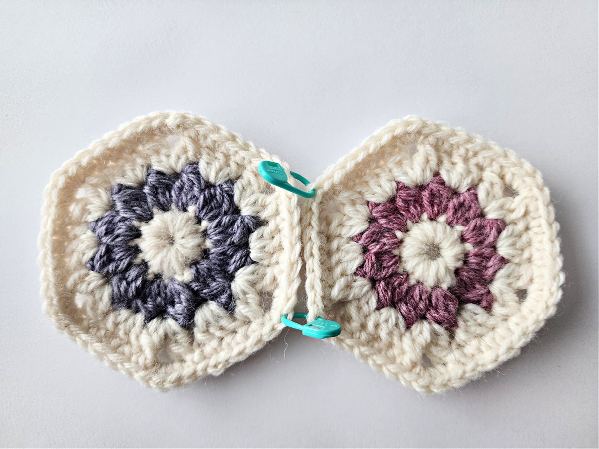 Cream, purple and pink crochet hexagons held together with stitch markers.