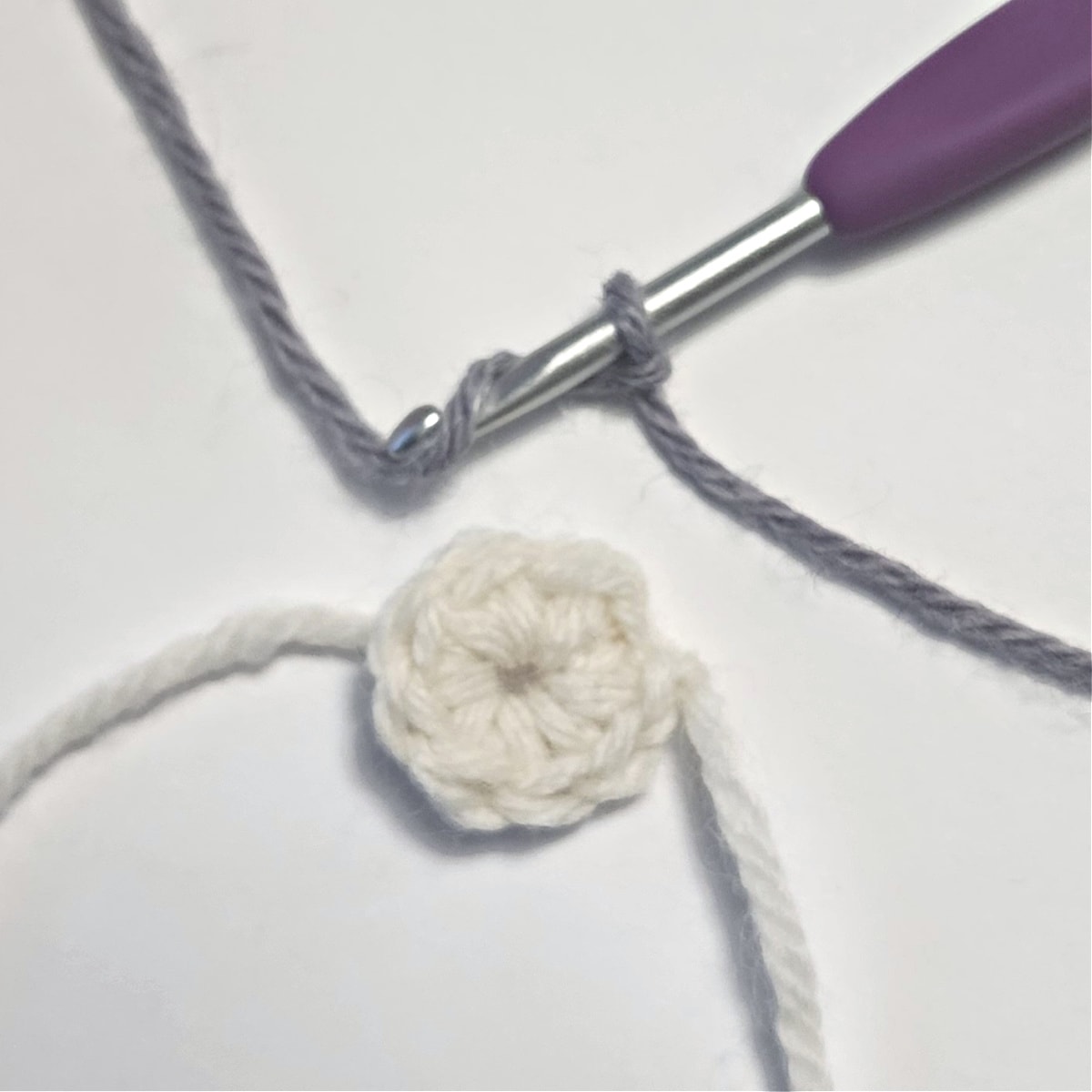 Small crochet circle with crochet hook and yarn to begin a double crochet cluster stitch.