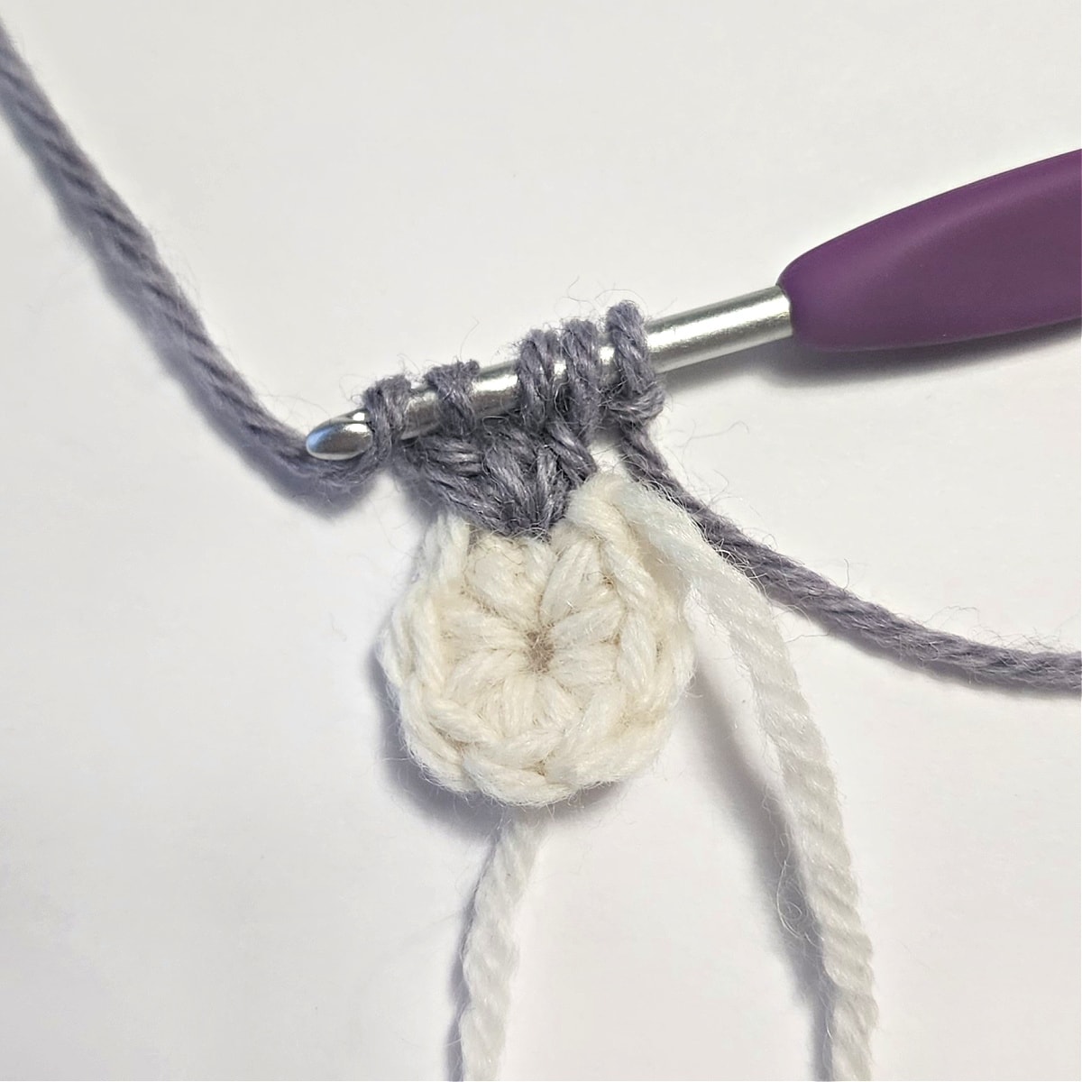Small crochet swatch with a purple crochet hook and cluster stitch being worked.