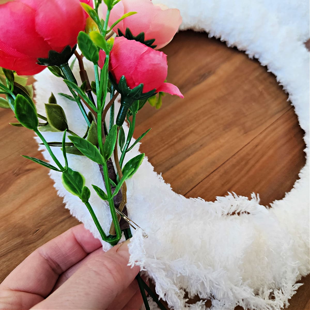 Yarn needle and white yarn attaching small sprig of flowers to crochet wreath.