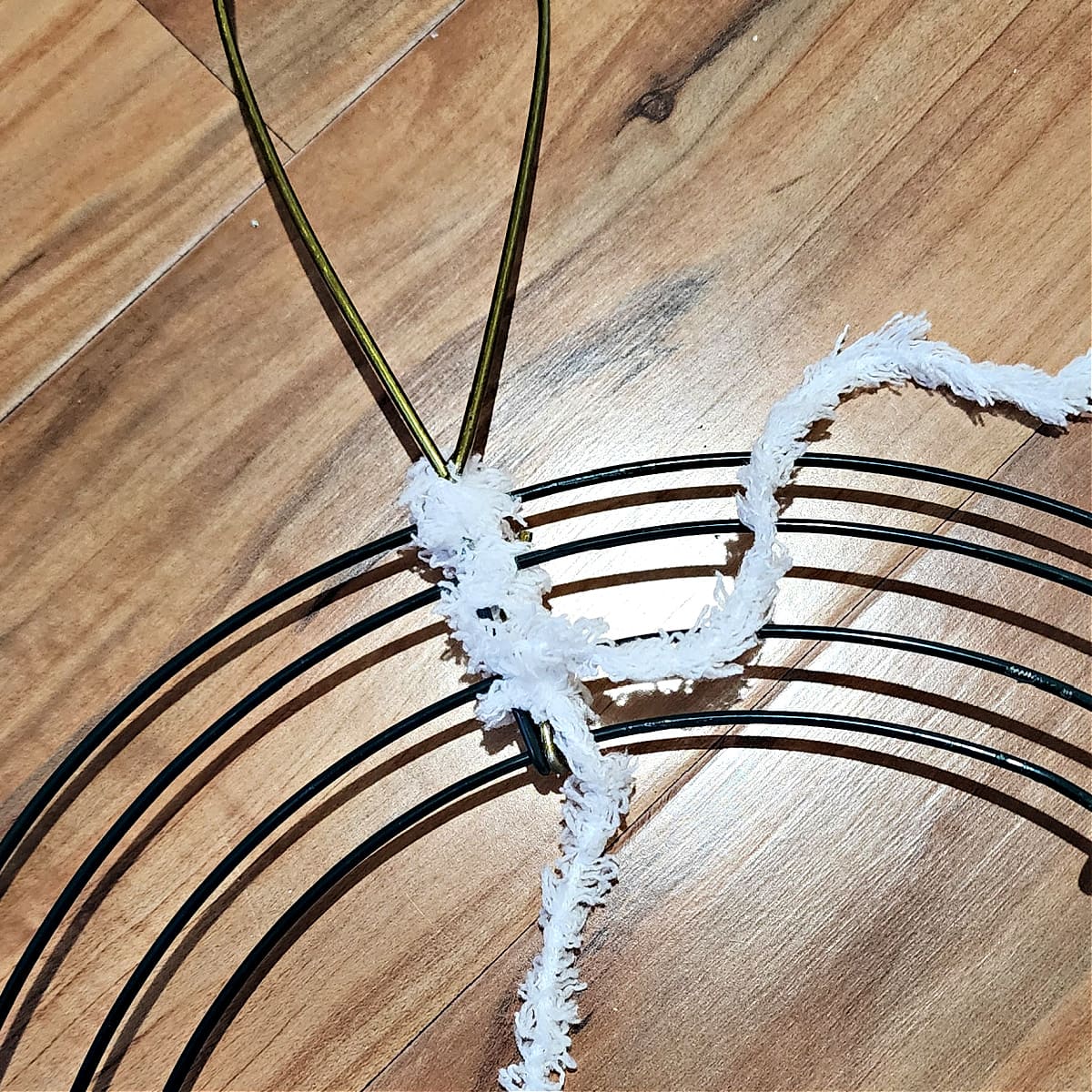 Yarn being wrapped around end of bunny ear and wire wreath form to secure bunny ear.