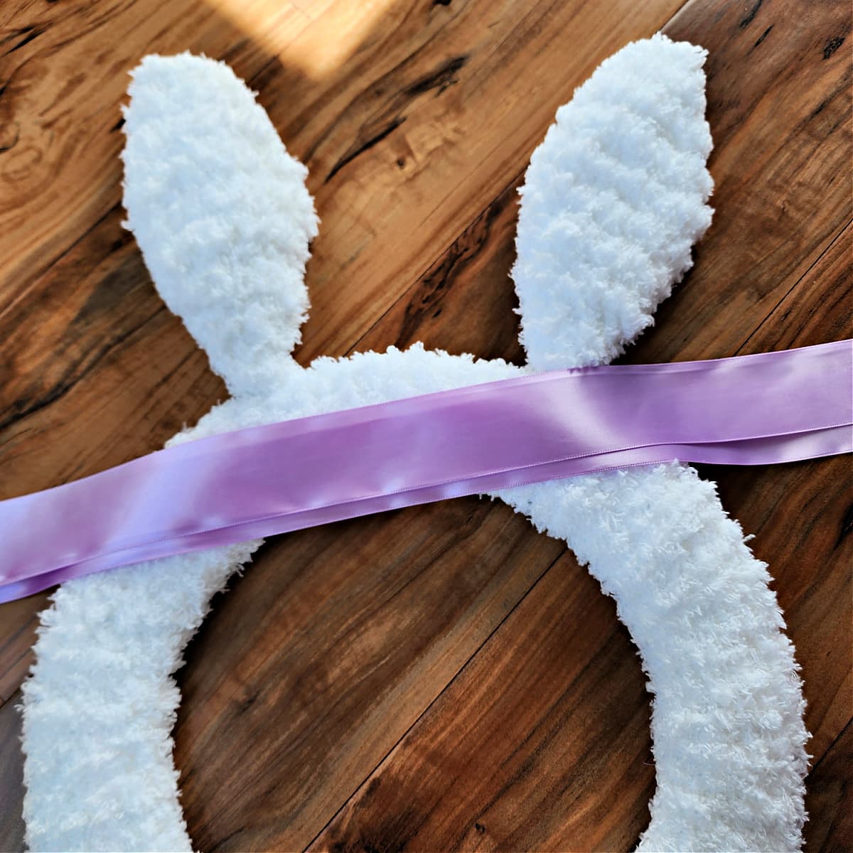 Two pieces of purple satin ribbon laying on crochet bunny wreath.