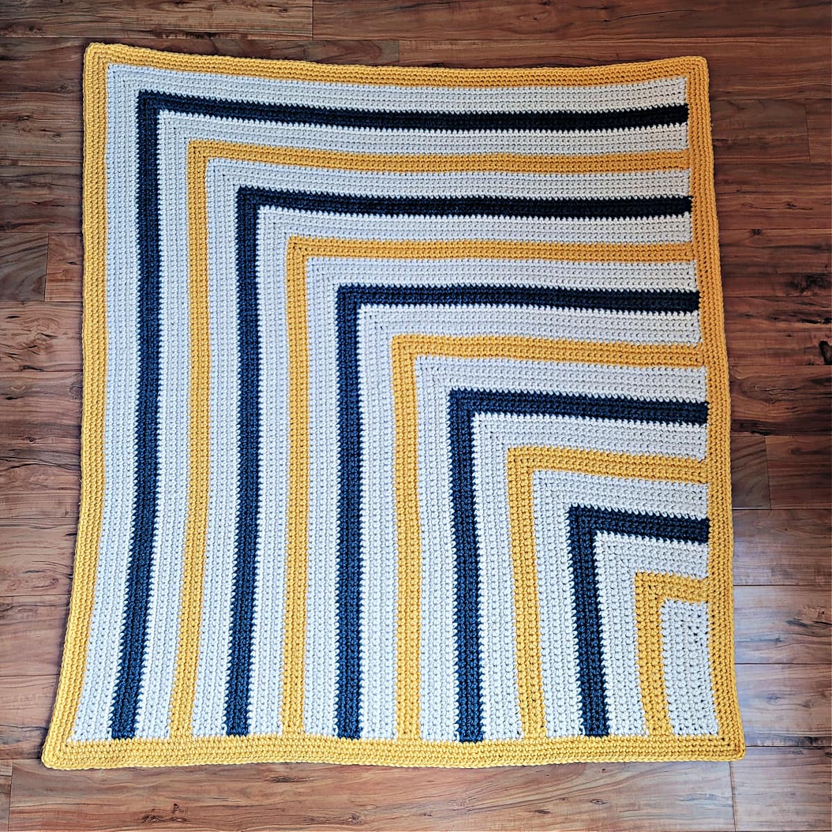 A chunky crochet blanket spread out on a wood floor.