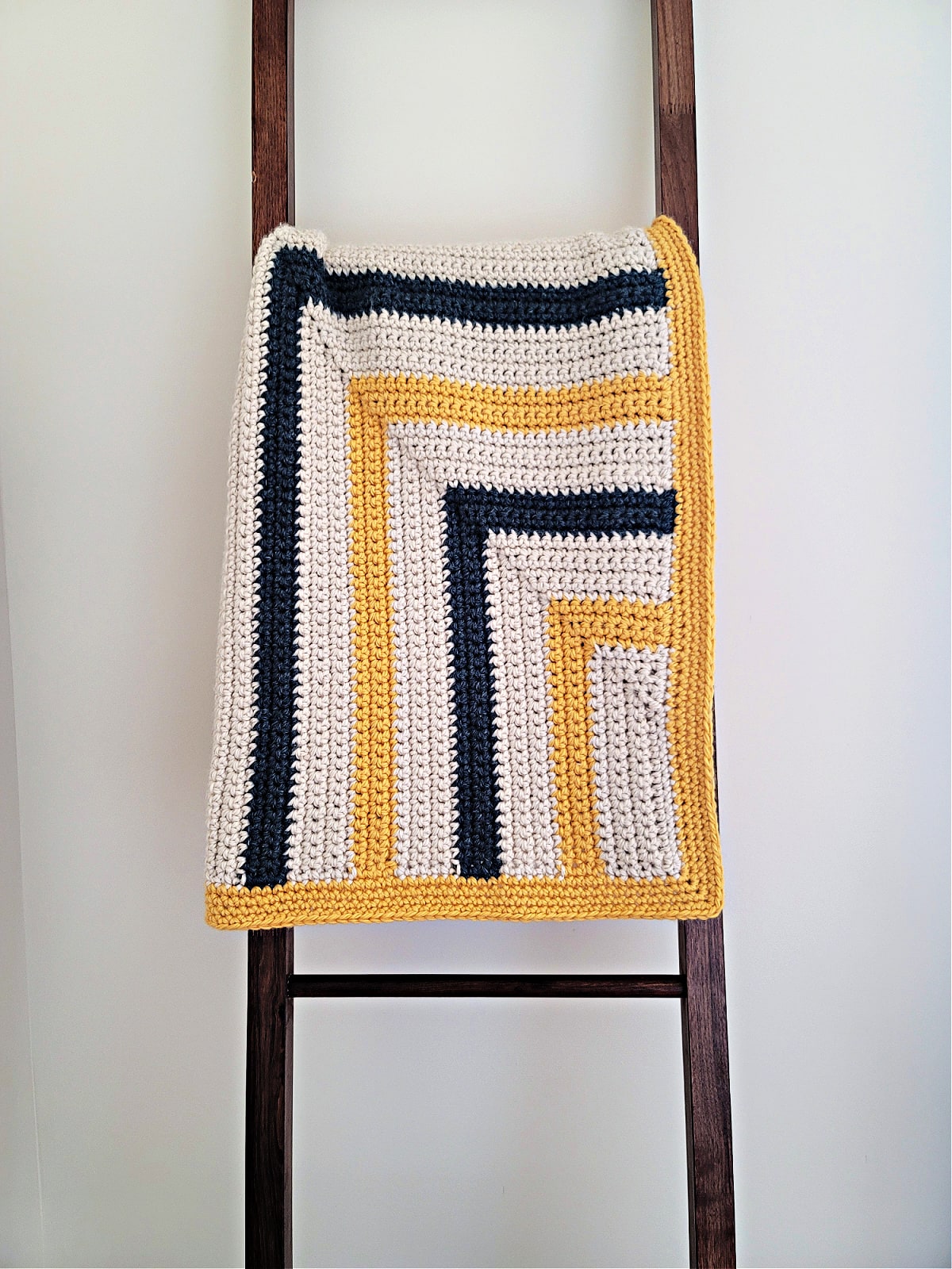 A chunky striped crochet blanket folded and draped over a wood blanket ladder.