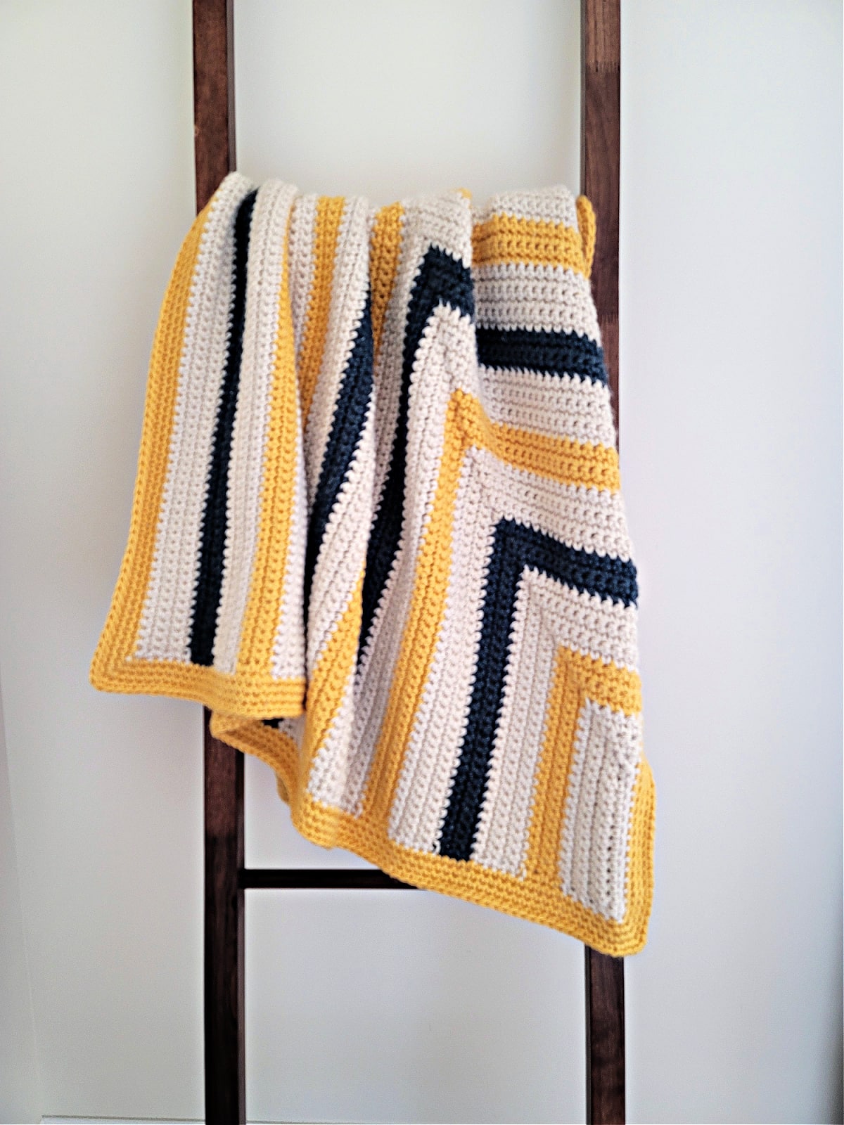 A chunky crochet blanket draped over a brown wood blanket ladder.