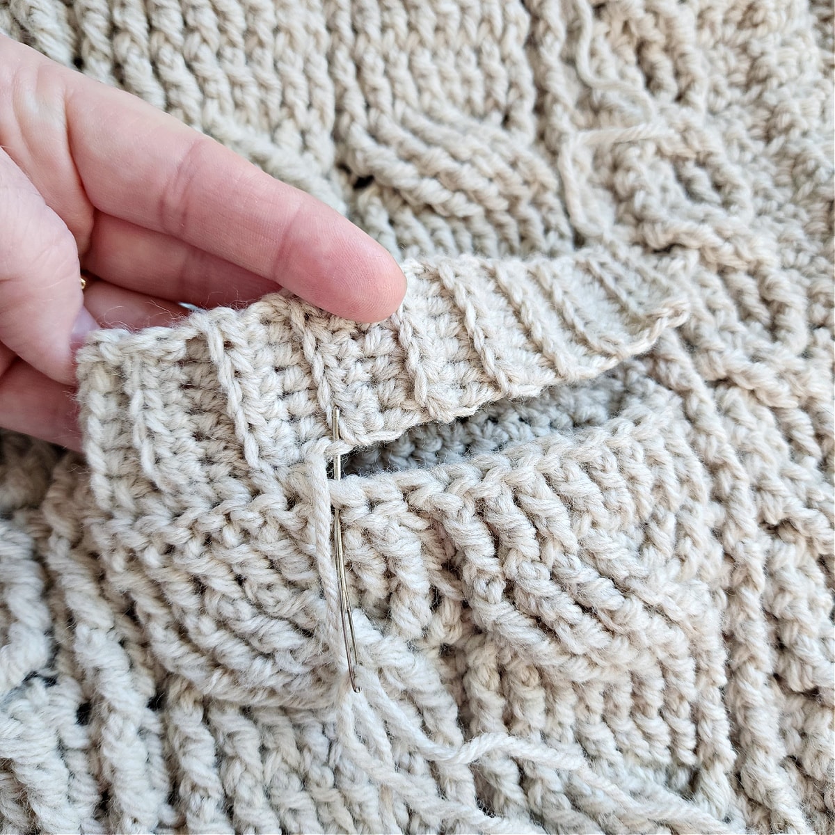 Crochet ribbing being sewn onto pocket opening with yarn needle and tail of yarn.