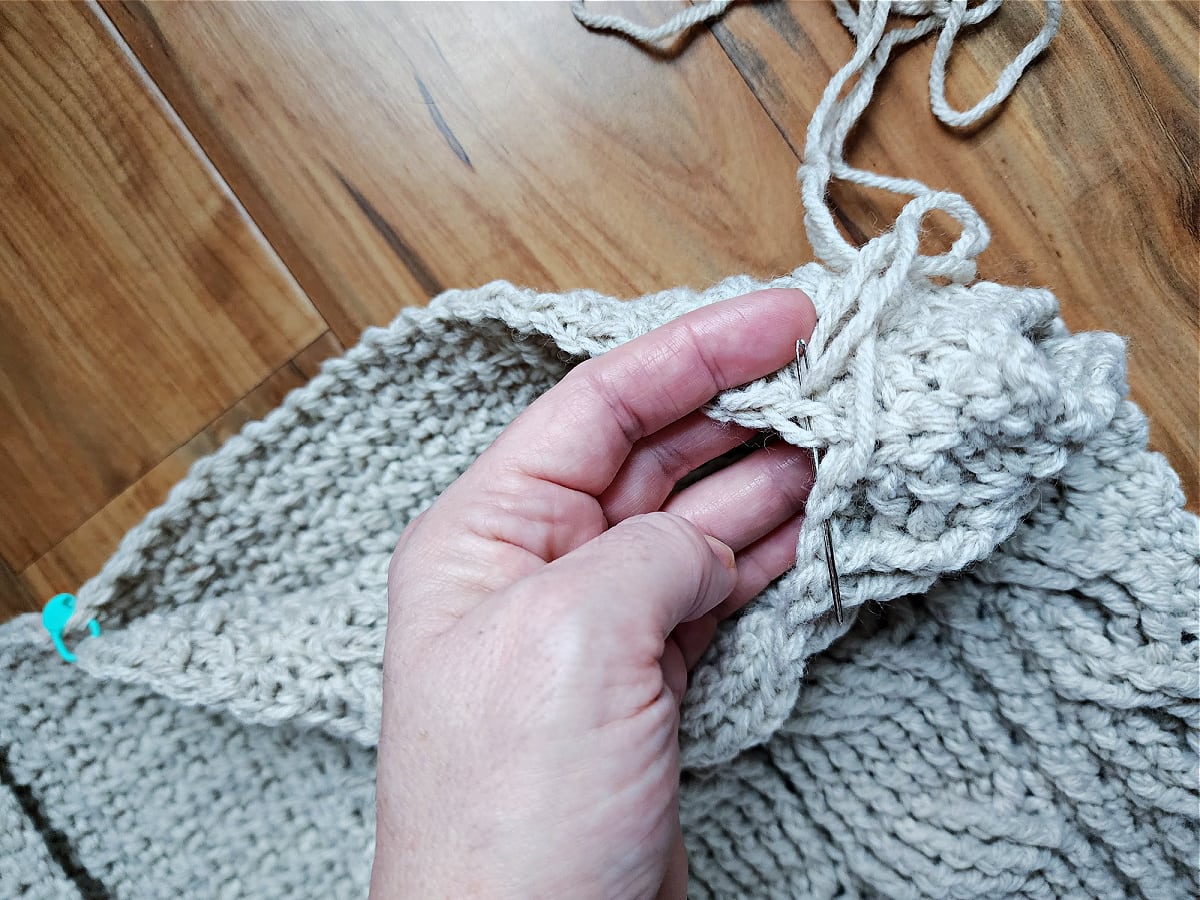 Hand holding shoulders of cardigan and seaming with whipstitch and yarn needle.