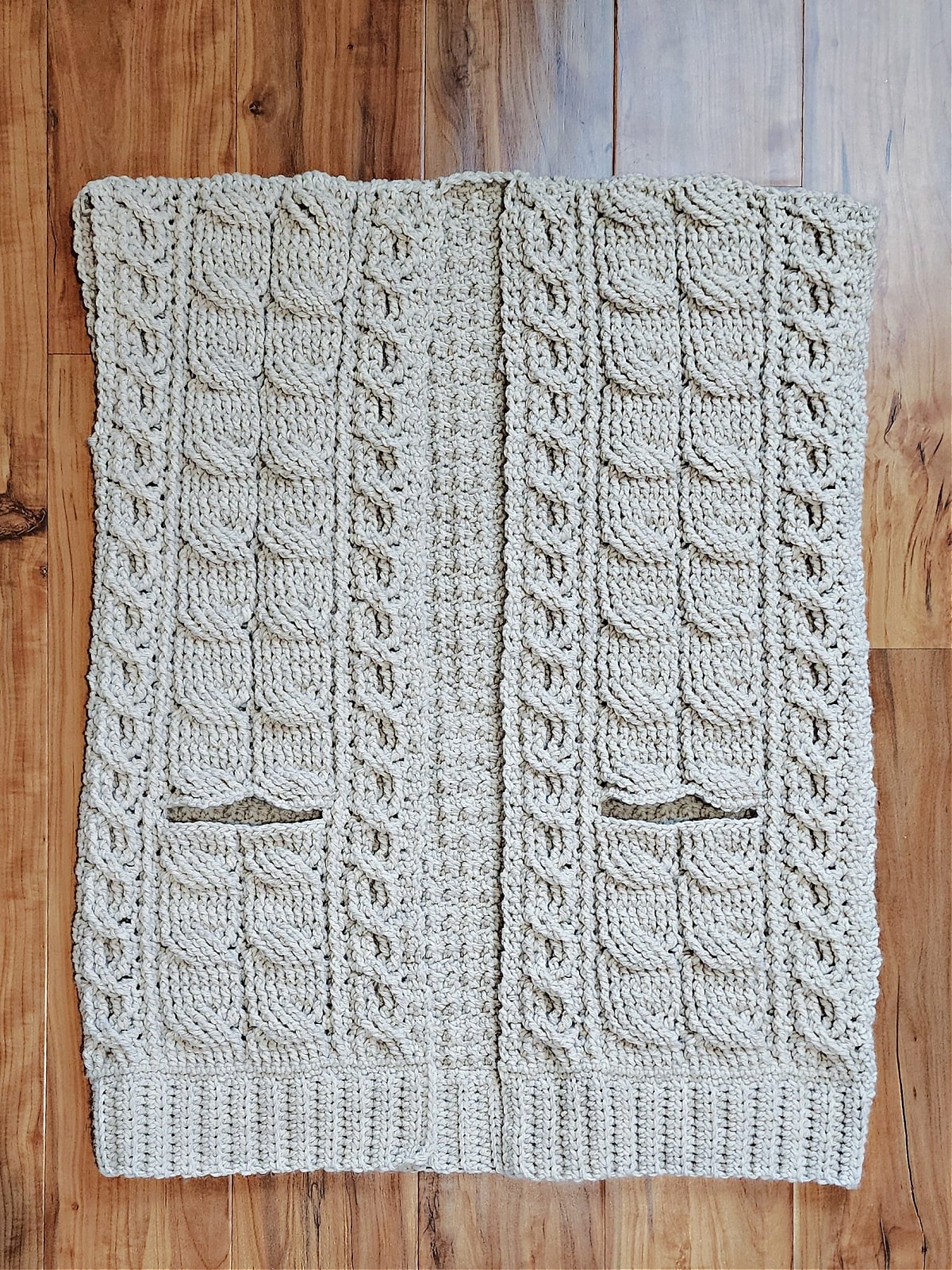 Body of crochet cable cardigan with shoulders seamed laying on wood floor.