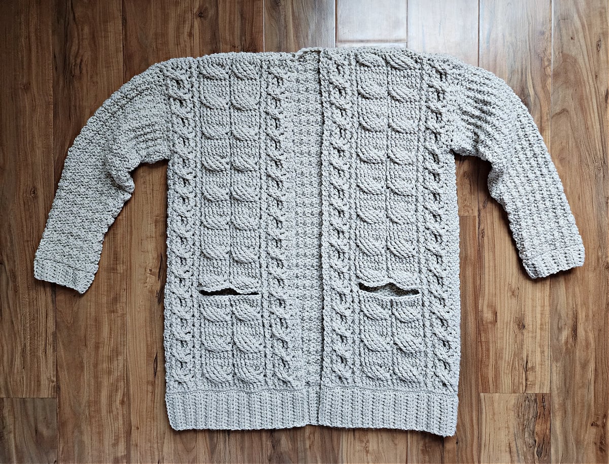 Crochet cable cardigan with both sleeves complete and laying flat on wood floor.