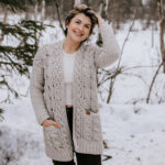 Woman wearing light taupe cabled cardigan running fingers through her short hair.