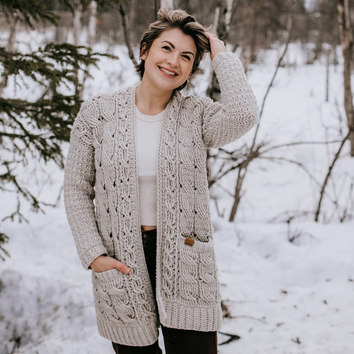 Woman wearing light taupe cabled cardigan running fingers through her short hair.