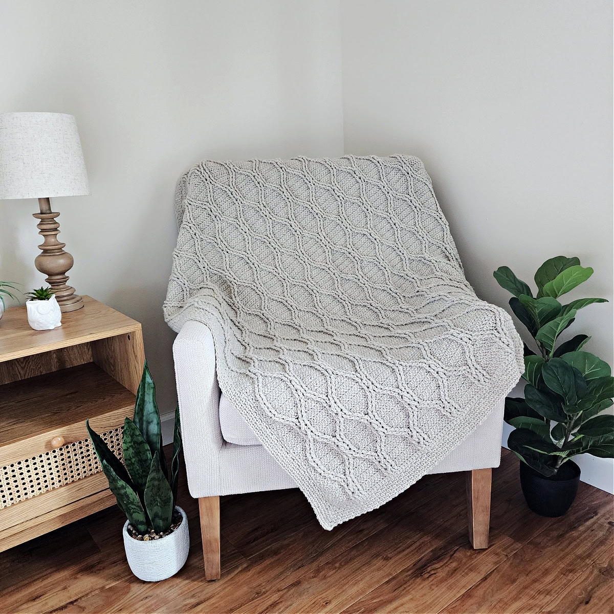 Light taupe crochet cable throw draped across a small armchair with plants next to it.