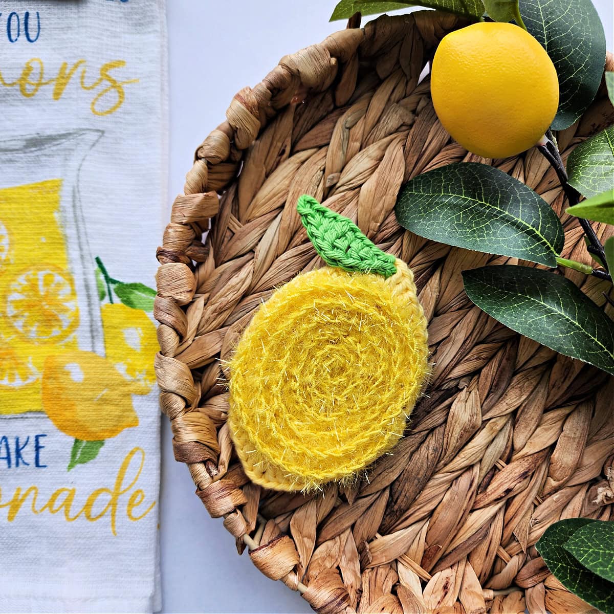 Crochet lemon dish scrubby laying on hibiscus tray with lemon branch and lemon towel.