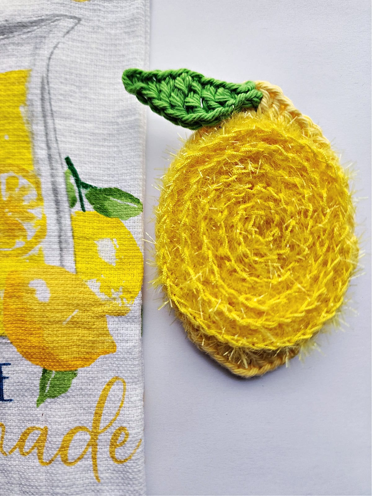 Lemon crochet dish scrubby laying next to a kitchen hand towel.