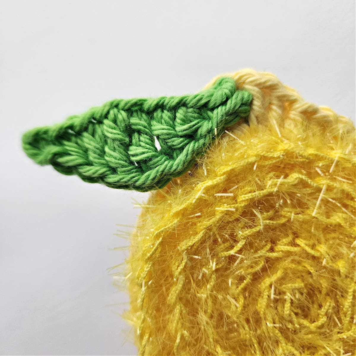 Crochet lemon leaf attached to the end of a crochet lemon.