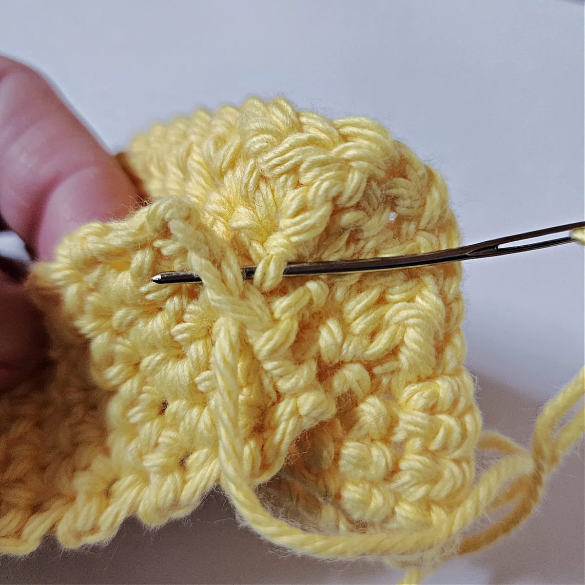 Yarn needle attaching the finger loop tp the back of the crochet lemon dish scrubby.