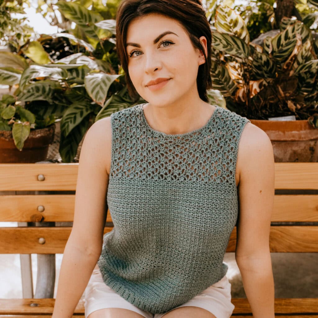 A woman wearing a green crochet summer top sitting on a bench.