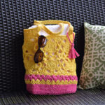 Flower motif crochet tote bag in yellow and pink sitting on a porch swing.