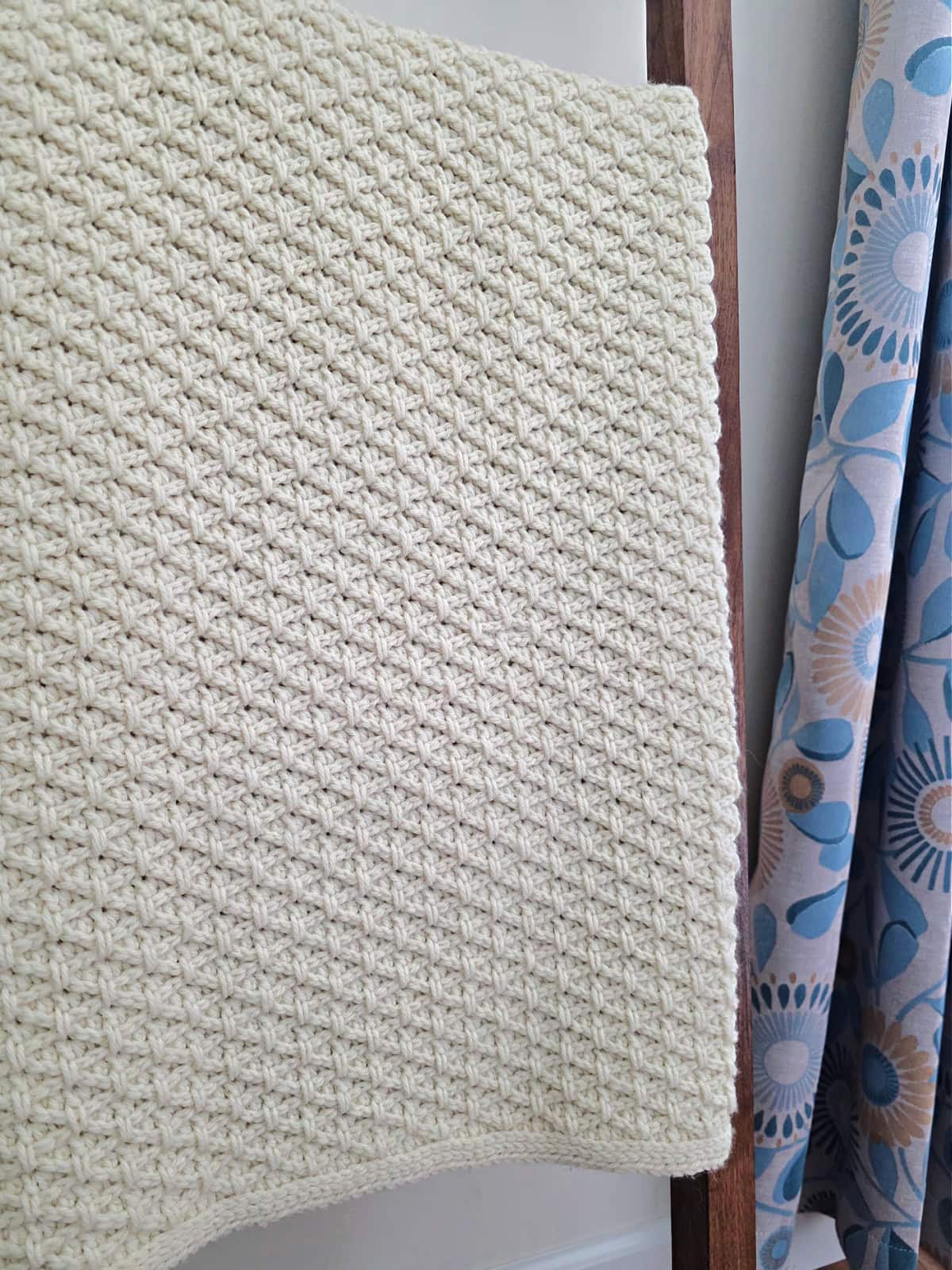 A crochet blanket pattern folded and hanging on a wood blanket ladder.