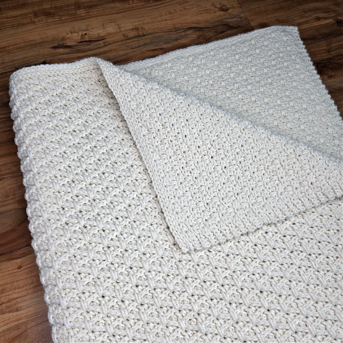 A crochet blanket pattern folded and laying on a wood floor with one corner turned back.