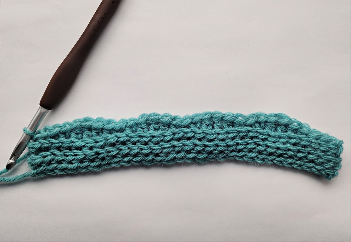 A small green knit-look crochet swatch and a brown crochet hook.