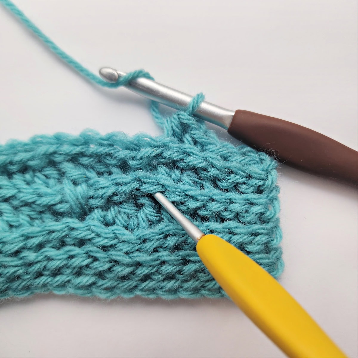 A yellow crochet hook showing where to work a double crochet stitch two rows below.