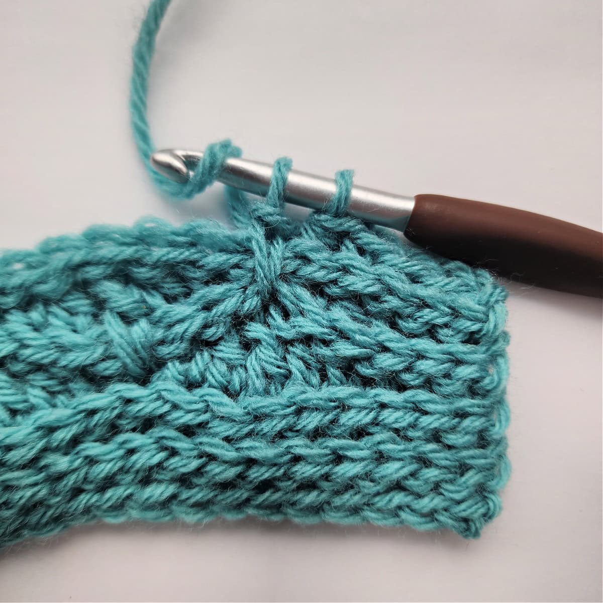 A close-up of a double crochet stitch being worked into a double crochet stitch two rows down.