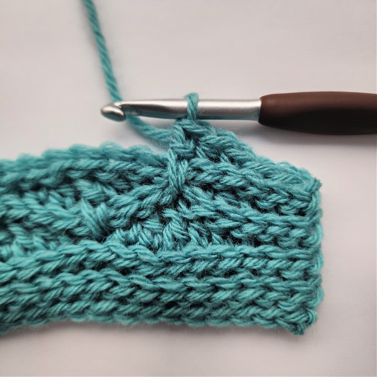 A close-up of a double crochet stitch worked into a double crochet stitch two rows down.
