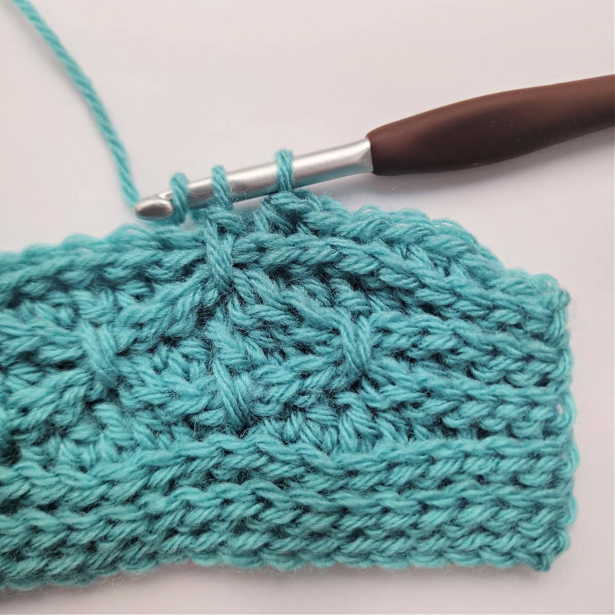 A close-up of a double crochet stitch being worked into a double crochet stitch two rows down in row 11.