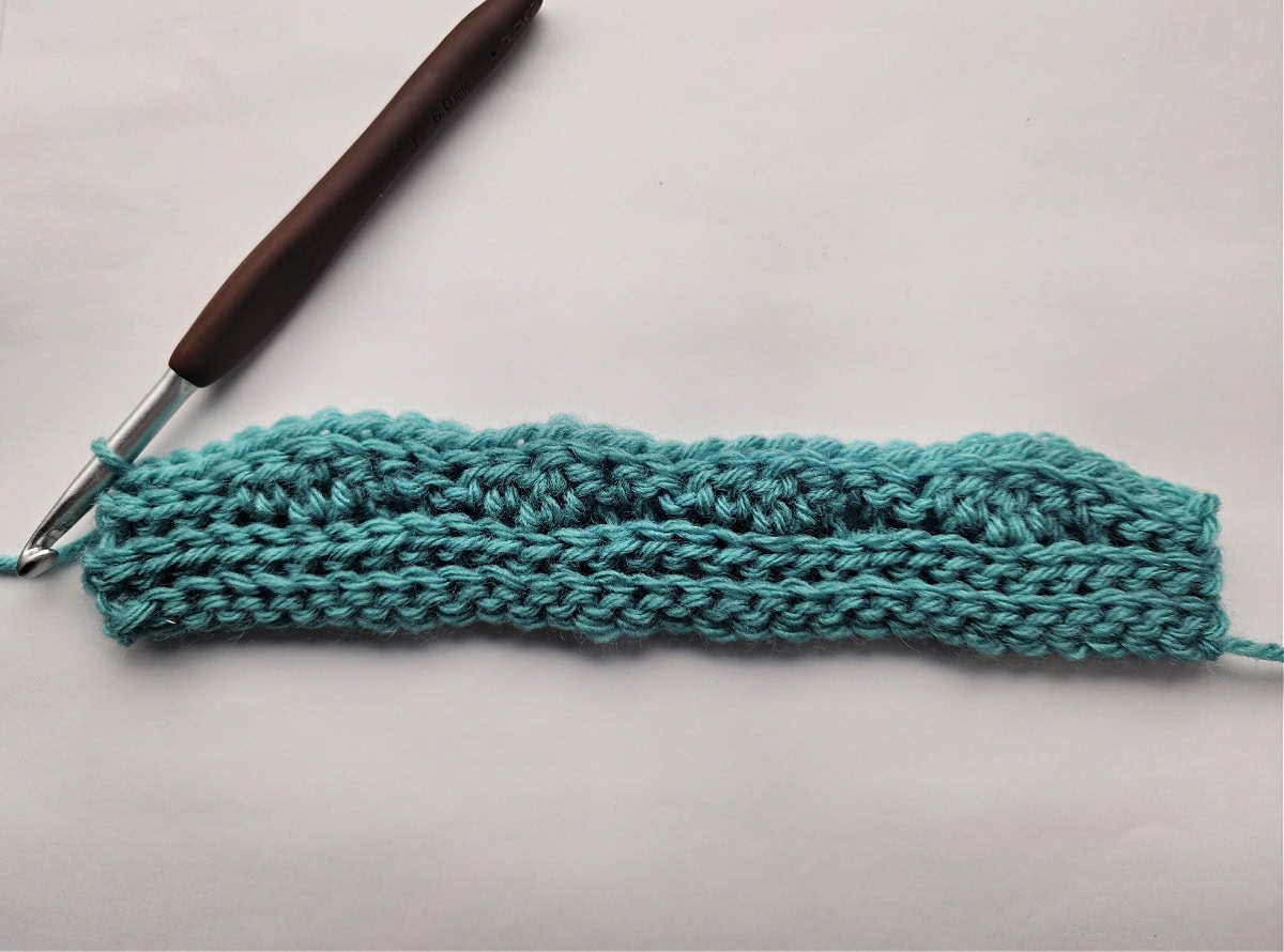 A green knit-look crochet swatch and a crochet hook.