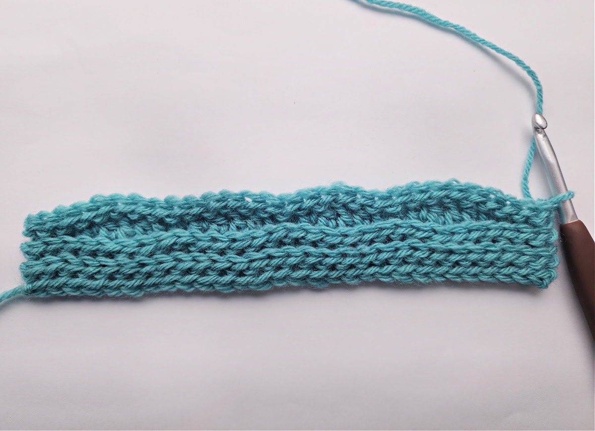 A small knit-look crochet swatch and a brown crochet hook.