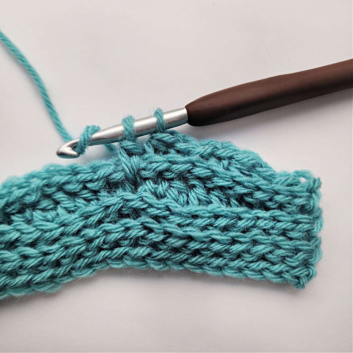 Close-up of a double crochet stitch being worked a couple rows down.