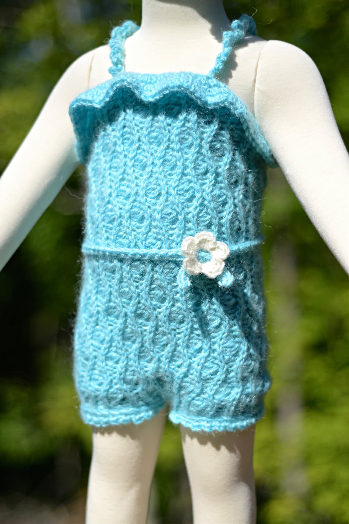 Baby mannequin standing outdoors with a blue crochet romper.