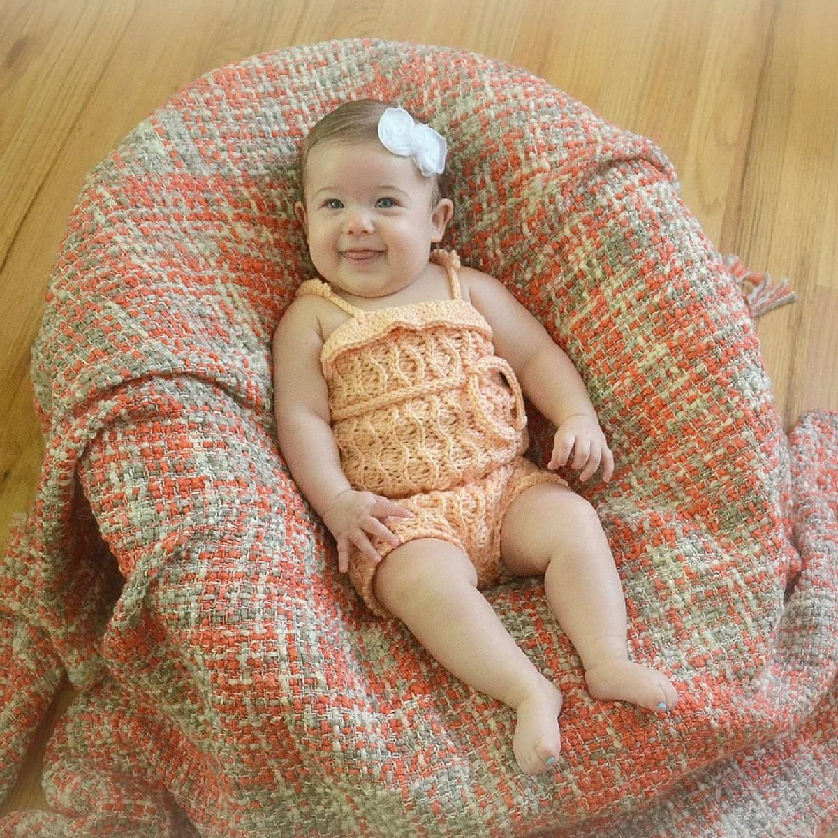 Baby in a chair wearing a peach colored crochet romper.