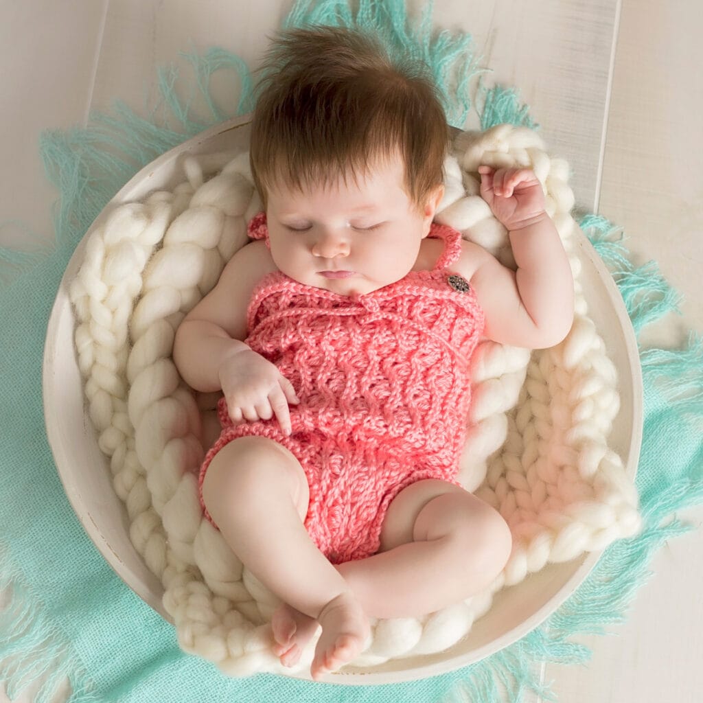 Baby in a basket wearing a pink crochet romper.