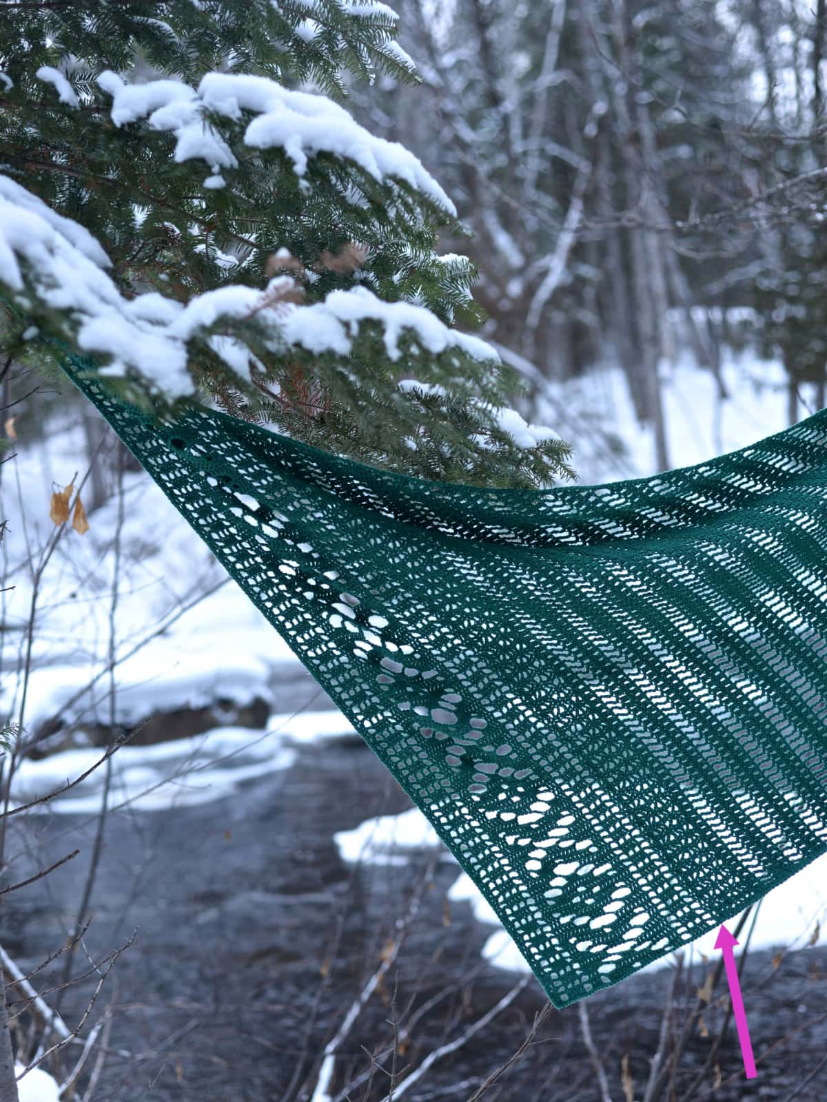 A green crochet shawl draped over a tree in a snowy area.