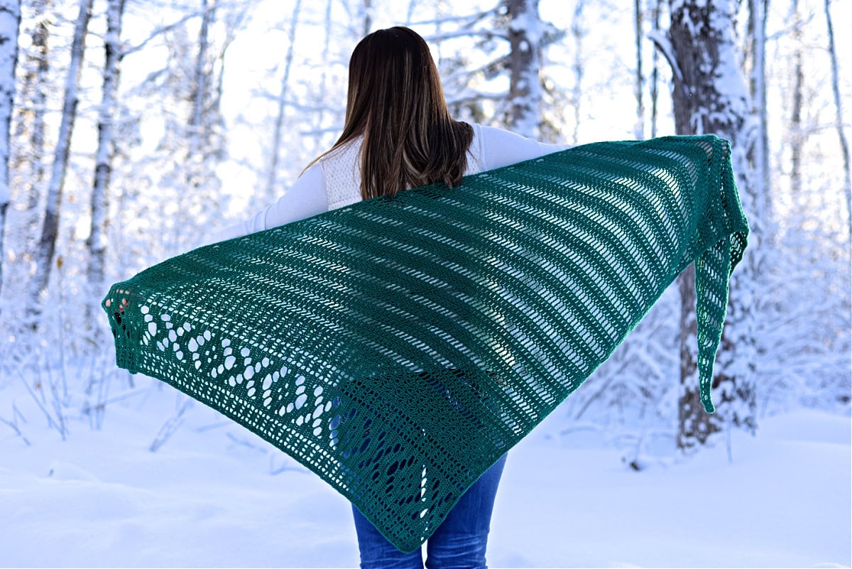 Woman with her back to the camera stretching out a green crochet shawl.