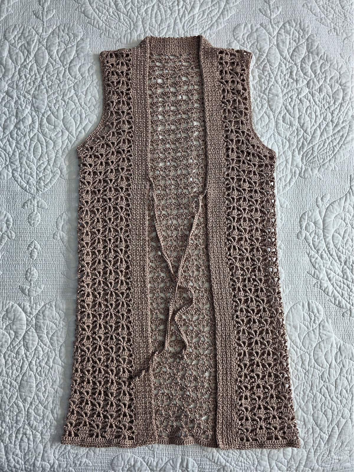 A women's crochet summer vest complete and laying on a white bedspread.