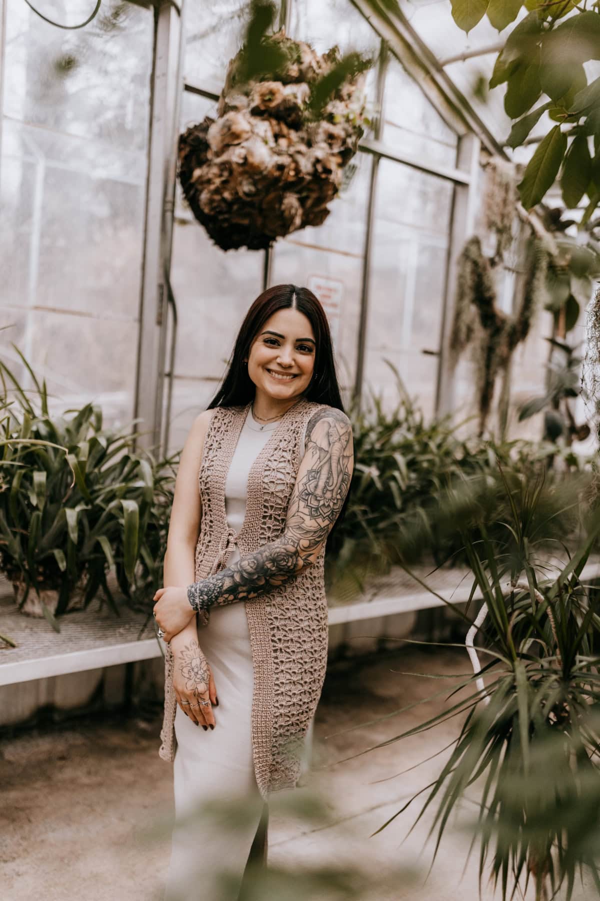 A women wearing a long crochet summer vest standing in a greenhouse.