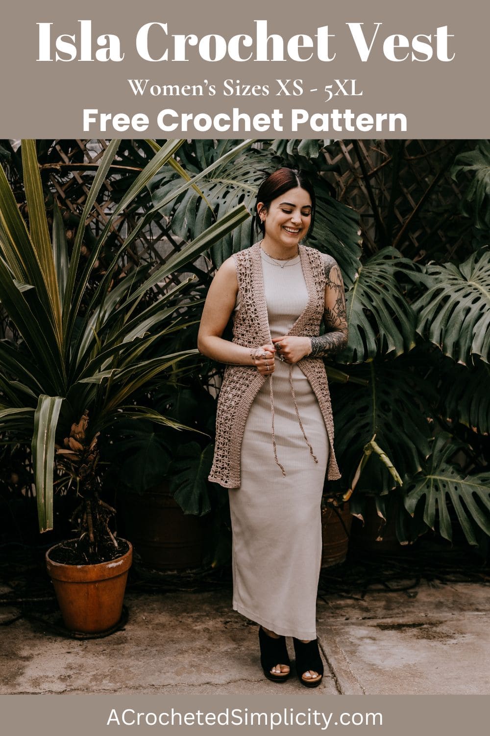 A young women wearing a long crochet summer vest over a knit dress standing in front of large greenery.