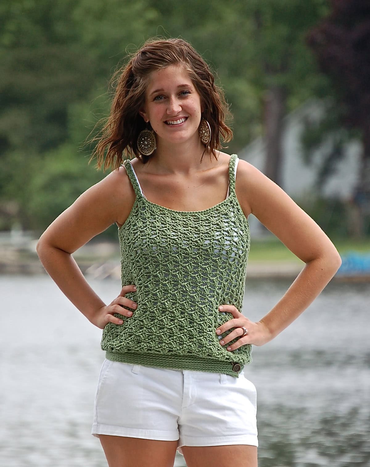 Woman wearing a green crochet tank top with her hands on her waist standing in front of a lake.