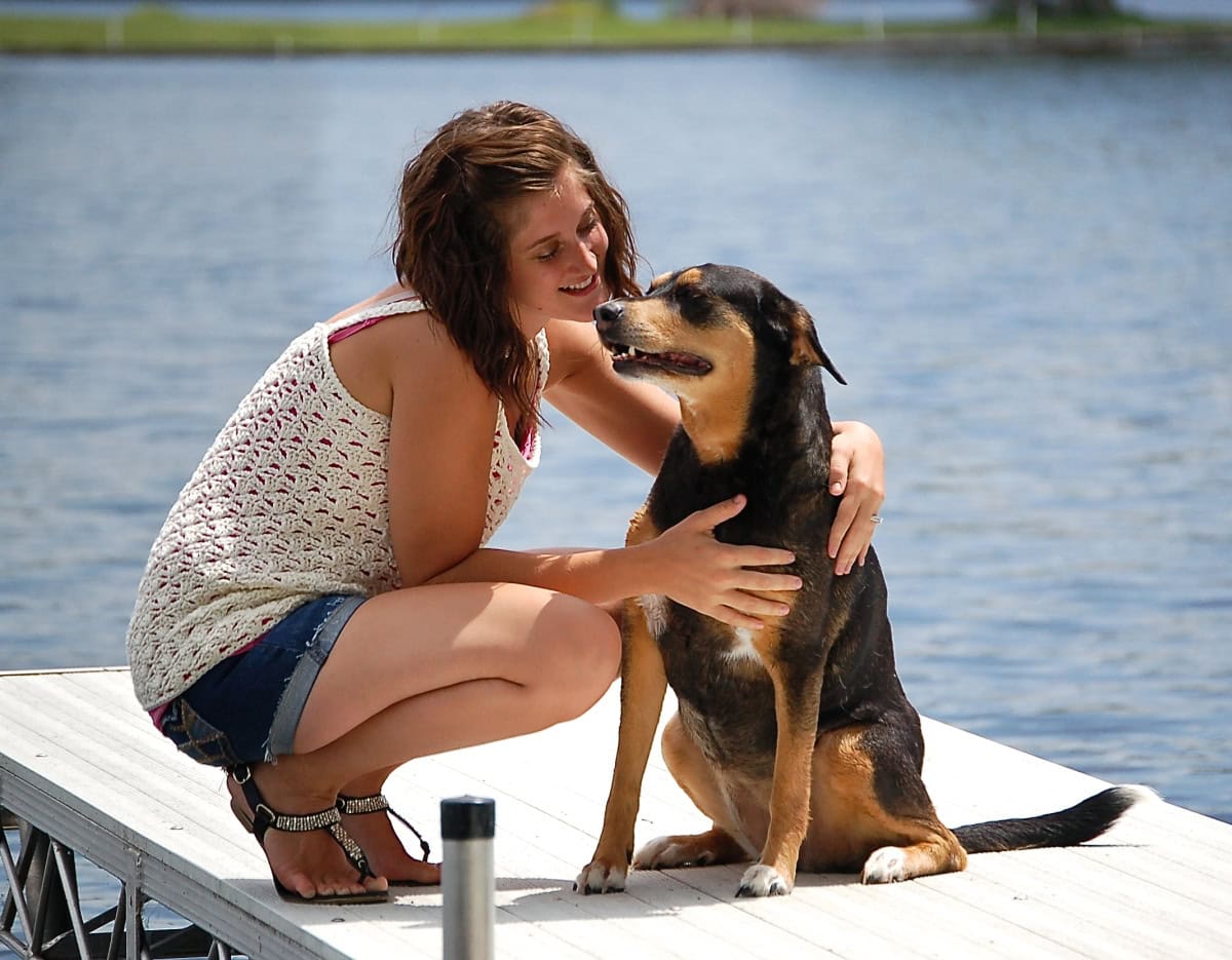 Woman wearing a white crochet tank top with dog in front of a lake.