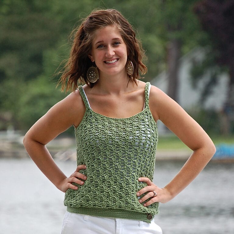 Woman wearing a green crochet tank top with her hands on her waist standing in front of a lake.