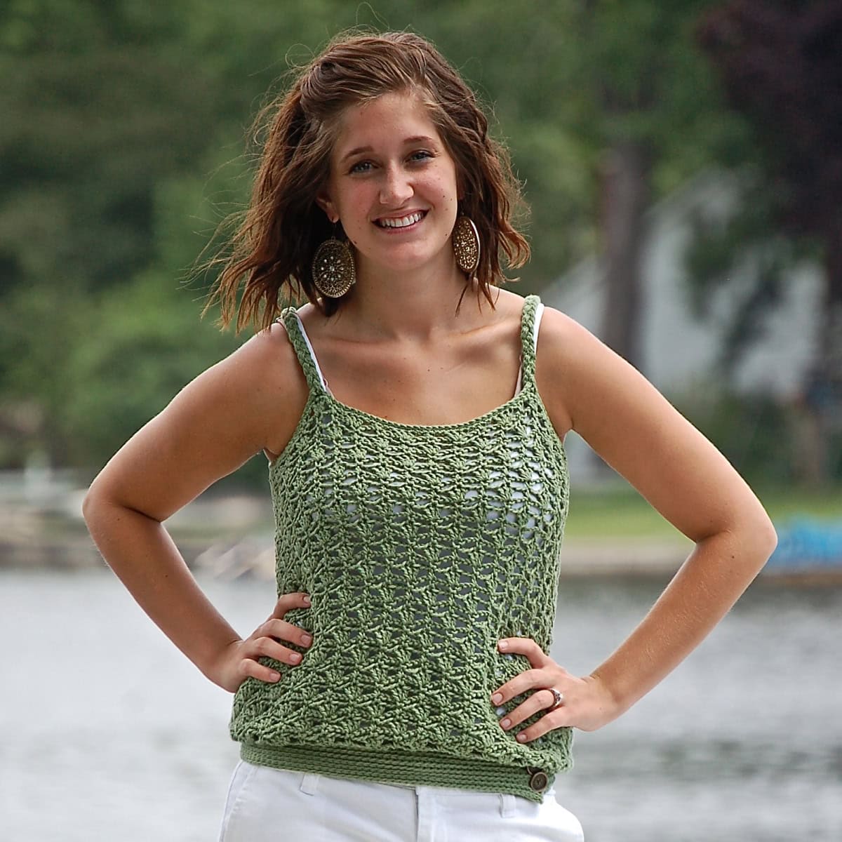 Woman wearing a green crochet tank top with her hands on her waist standing in front of a lake.