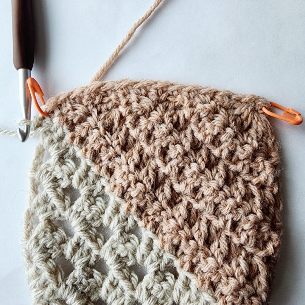Granny square motif with stitch markers in each corner and a crochet hook inserted into a stitch.