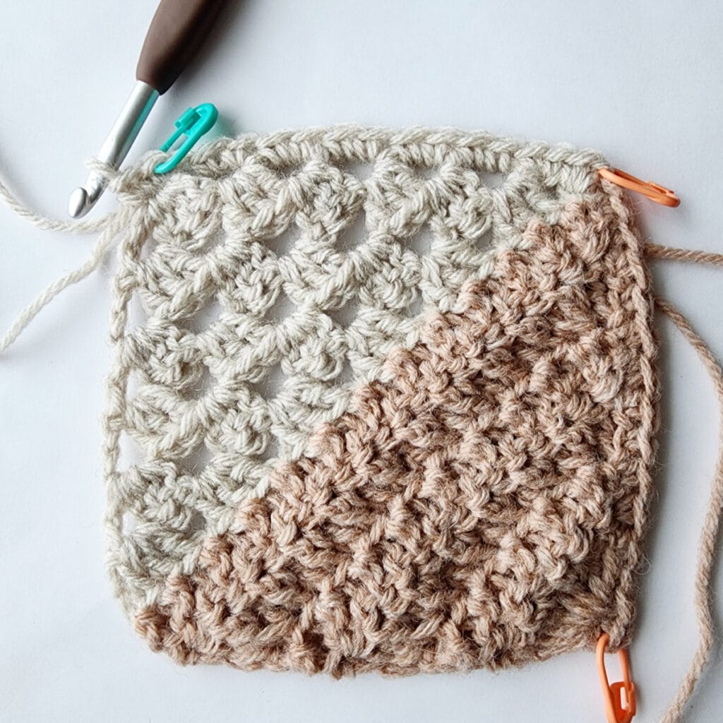 Granny square motif with stitch markers in the corners and a crochet hook inserted into a stitch.