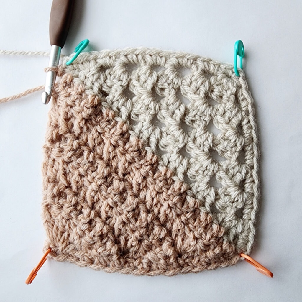 Granny square motif with stitch markers in each corner and a crochet hook inserted into a stitch.