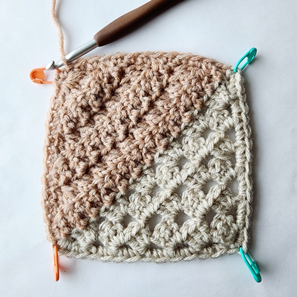 Granny square motif with stitch markers in each corner and a crochet hook inserted into a stitch.