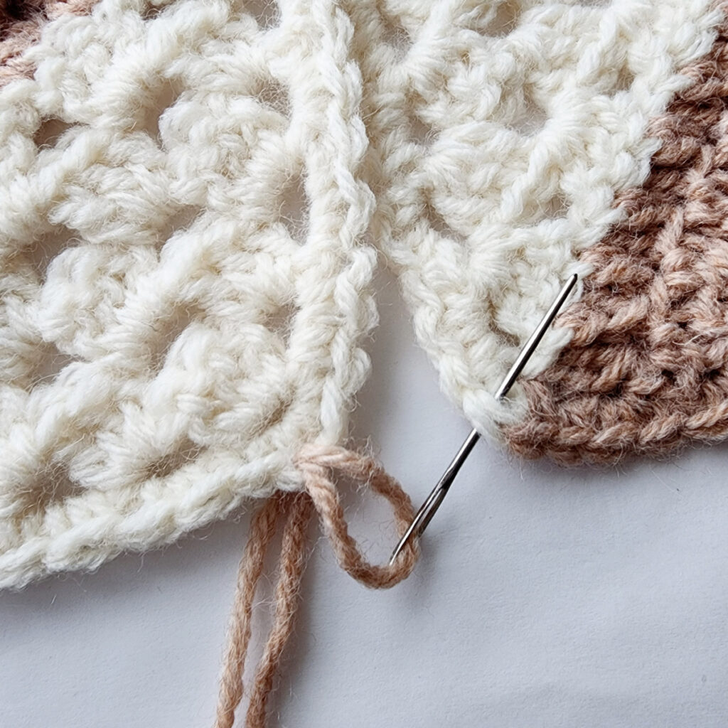 Seaming two crochet granny square motifs with a needle.