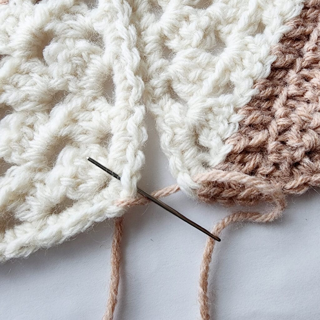 Seaming two crochet granny square motifs with a needle.